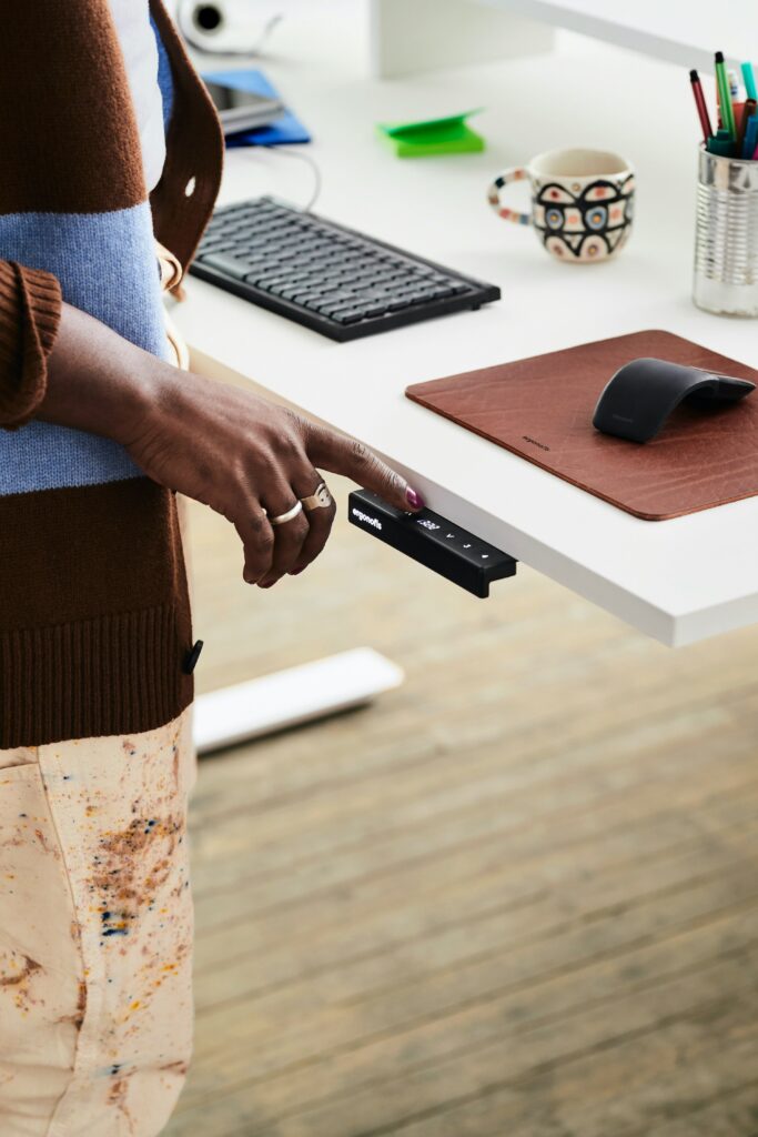 Hand pressing the height adjustment button on a standing desk control panel