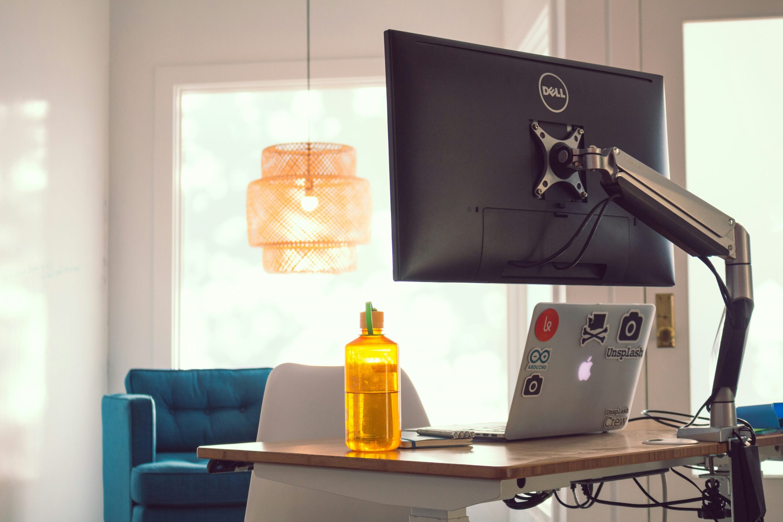 Gas spring monitor arm holding a Dell monitor above a laptop on a standing desk in a bright home office