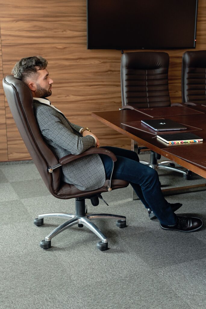 Professional man sitting in a leather executive office chair at a boardroom table in a corporate meeting room