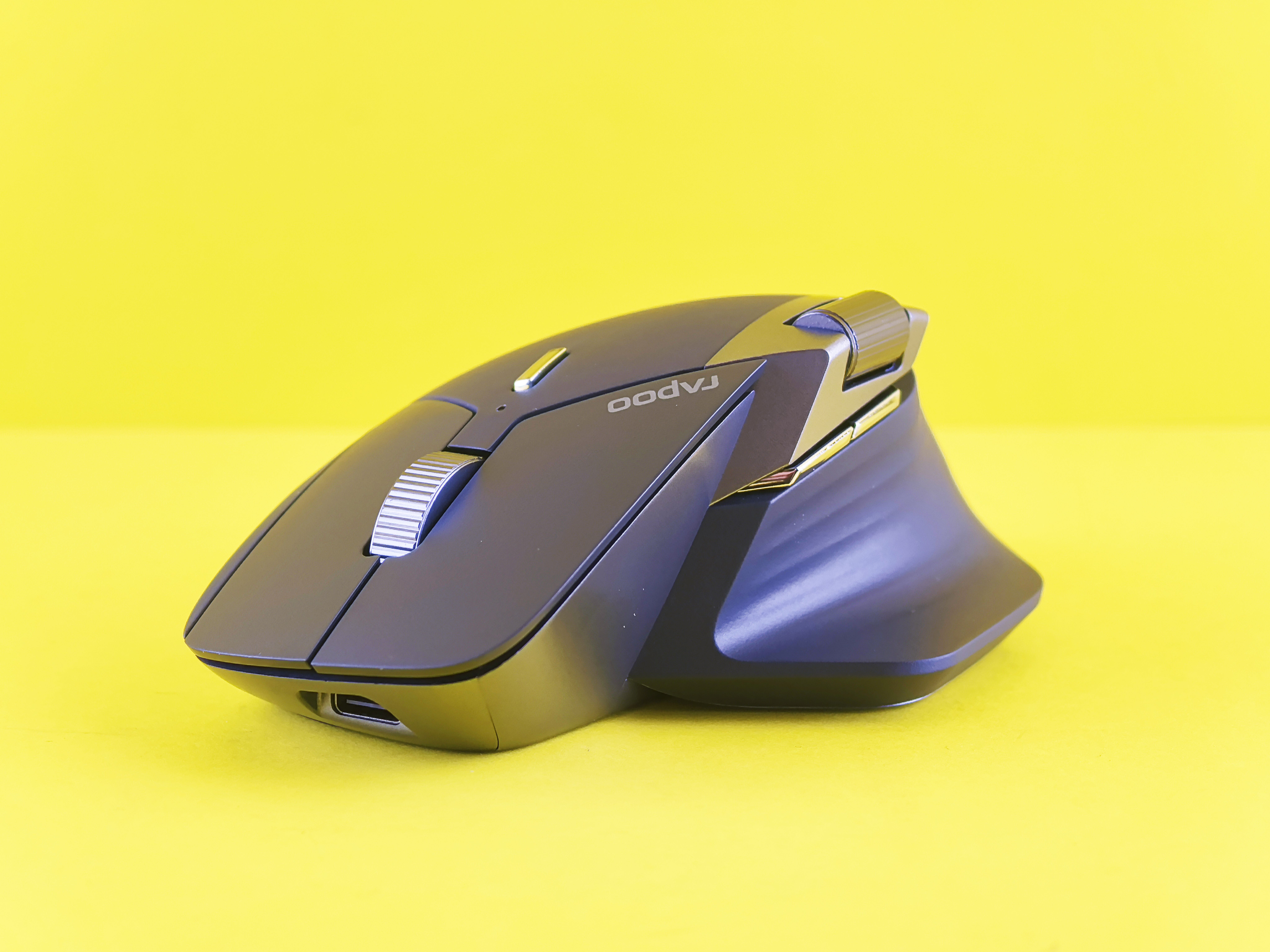 Vertical ergonomic wireless mouse with a raised thumb rest and scroll wheel, shown against a yellow background